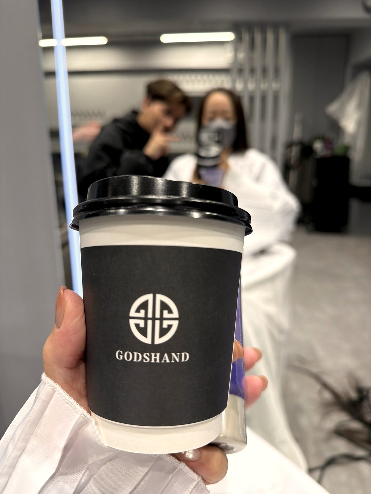 Branded Godshand coffee cup held by a guest in the salon